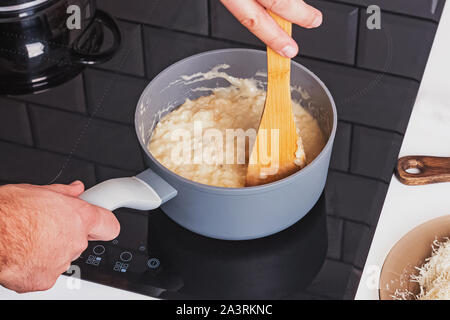 La miscelazione manuale cremoso risotto con formaggio in una pentola di close-up. L'uomo cucinare la cena a casa Foto Stock