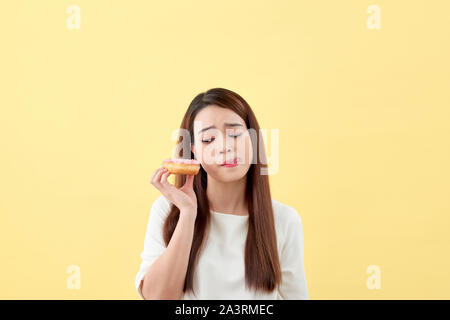 Ritratto di un felice giovane donna asiatica di mangiare le ciambelle isolate su sfondo giallo Foto Stock