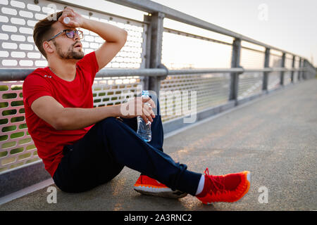 L'uomo runner prendendo una pausa durante il corso di formazione all'esterno. Appoggio del pareggiatore dopo l'esecuzione. Foto Stock