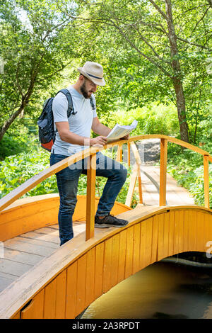 Giovane uomo escursionismo vivere sano stile di vita attivo. Uomo Barbuto viaggiatore con zaino legge una mappa all'aperto sullo sfondo della foresta. Estate vacat Foto Stock