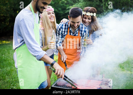 Gruppo di persone felici intorno permanente grill, chat, bere e mangiare. Foto Stock