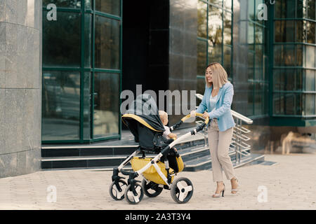 Ritratto di una donna d'affari di successo in tuta blu con il bambino. Business donna spingendo passeggino Foto Stock