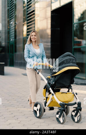 Ritratto di una donna d'affari di successo in tuta blu con il bambino. Business donna spingendo passeggino Foto Stock