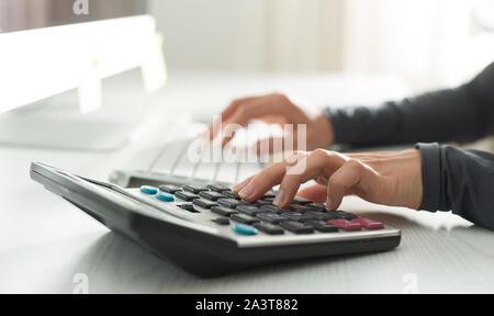 La mano di un ragioniere conta su una calcolatrice e scrive una relazione finanziaria. Foto Stock