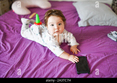 Piccolo bambino con un telefono. sul letto. conoscenza dei dispositivi mobili. Piccolo bambino con il telefono cellulare. Little baby in casuale coloratissimi capi di abbigliamento a righe con Foto Stock