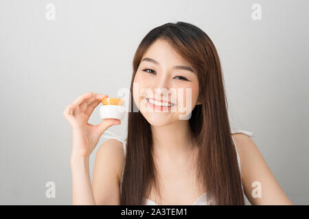 Sorridente giovane donna asiatica che mostra dermocosmesi prodotto. Concetto di bellezza. Foto Stock