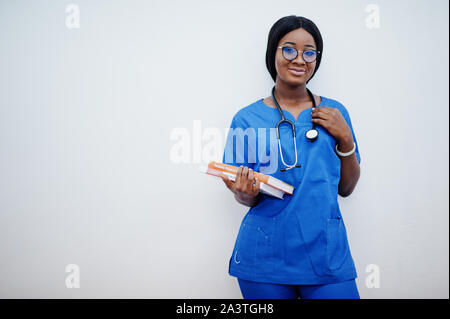 Ritratto di donna felice americano africano giovane medico pediatra in uniforme blu e il cappotto di uno stetoscopio con libri a mani isolato su bianco. Foto Stock