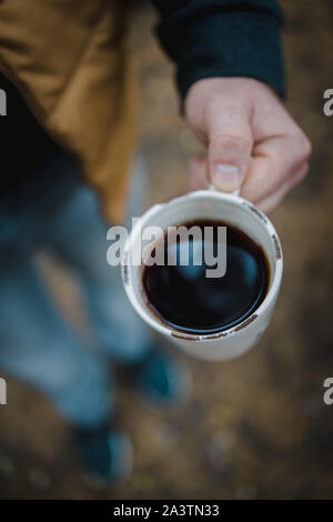 Un uomo detiene una tazza di tè con caffè su uno sfondo di foglie di autunno, vista dall'alto. Calda atmosfera autunnale, soft focus. Foto Stock