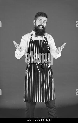 Siete i benvenuti. Uomo Barbuto con gesto di saluto indossando grembiule di bib. Allegro uomo cook con barba e baffi in cucina il grembiule. Elegante uomo cameriere o barista. Un uomo servo. Foto Stock