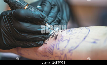 Professional tattoo artist fa un tatuaggio su una giovane mano d'uomo, close-up. Tattoo Artist facendo tattoo nel salone di tatuaggi. Processo di fabbricazione di un tatuaggio in compagnia TAT European Airlines Foto Stock