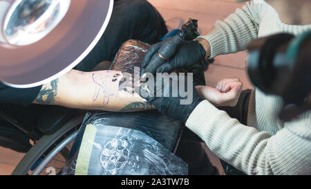 Professional tattoo artist fa un tatuaggio su una giovane mano d'uomo, close-up. Tattoo Artist facendo tattoo nel salone di tatuaggi. Processo di fabbricazione di un tatuaggio in compagnia TAT European Airlines Foto Stock