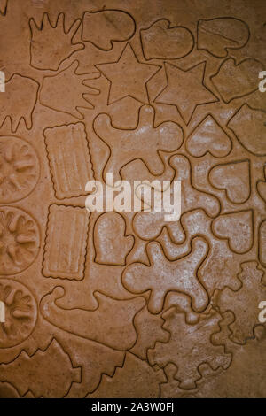 Tagliare gingerbread cookie nella forma di un albero di Natale, stella piccolo uomo, cuori da impasto crudo su pergamena carta da forno su uno sfondo scuro Foto Stock