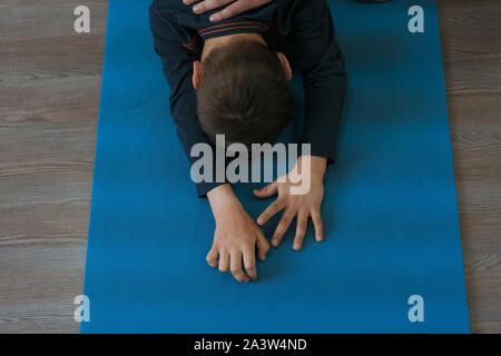 Little Boy è impegnata nella ginnastica su un materassino yoga, in piedi sulle ginocchia, età di circa 5 anni. Foto Stock