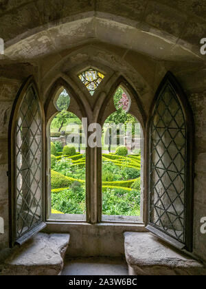 Finestra gotica di nicchia con panchine di pietra presso medieval Norbury Old Hall nel Derbyshire Regno Unito con vista sul delizioso giardino parterre Foto Stock