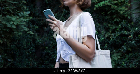 Schermata bianca vuota carrello tela sacchetto di panno e smartphone in azienda femmina mockup e il modello isolato sfondo naturale Foto Stock