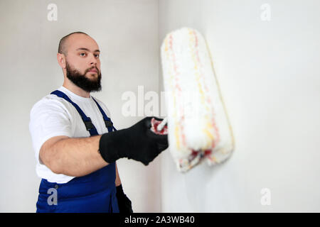 Operaio edile finitura facendo lavori di rinnovo nell'appartamento. Pittore professionista contraente utilizzando vernice bianca spazzola a rullo pittura del muro di cemento. Foto Stock