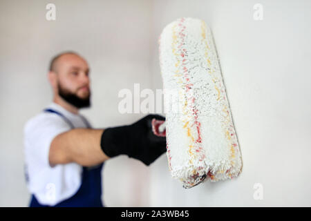 Operaio edile finitura facendo lavori di rinnovo nell'appartamento. Pittore professionista contraente utilizzando vernice bianca spazzola a rullo pittura del muro di cemento. Foto Stock