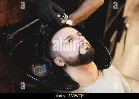 In un barbiere, un uomo è lavato i suoi capelli. Barbiere lava il suo cliente. Lavare i capelli e la barba dopo il taglio. La cura personale Foto Stock