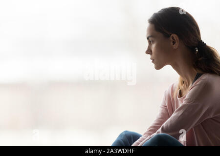 Riflessivo pensieroso ragazza seduta da solo guardando attraverso la finestra Foto Stock