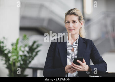 Ritratto di femmina senior business executive tenendo uno smartphone Foto Stock