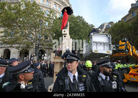 Un cherry picker si sposta in posizione, mentre i manifestanti occupano una struttura in legno sull'isola di traffico tra Northumberland Avenue e il filamento in Trafalgar Square durante il quarto giorno di una ribellione di estinzione (XR) protesta in Westminster, Londra. Foto Stock