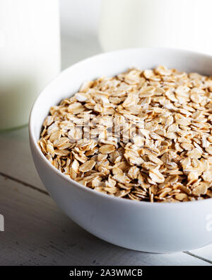 Fiocchi d'avena o fiocchi di avena nella ciotola con bottiglia di latte su sfondo bianco Foto Stock