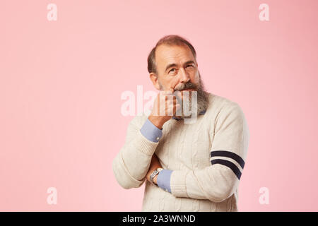 Ritratto di uomo anziano con barba grigia che indossa un maglione bianco cercando pensively su sfondo rosa Foto Stock