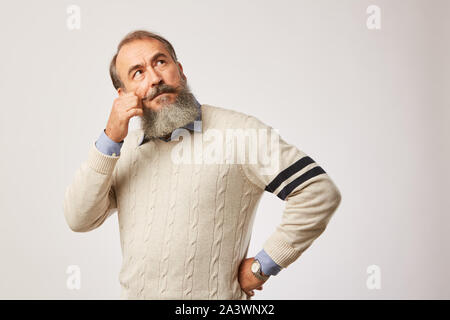 Ritratto di uomo anziano con la barba a pensare a qualcosa di permanente, mentre sullo sfondo bianco Foto Stock
