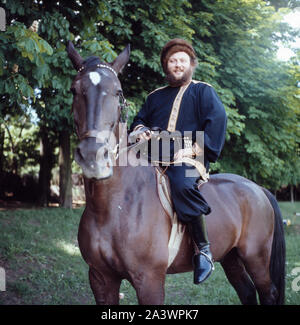 Der deutsche Bass Sänger Ivan Rebroff in traditioneller russischer Kleidung auf einem Pferd, Deutschland München Anfang 1980er. Foto Stock
