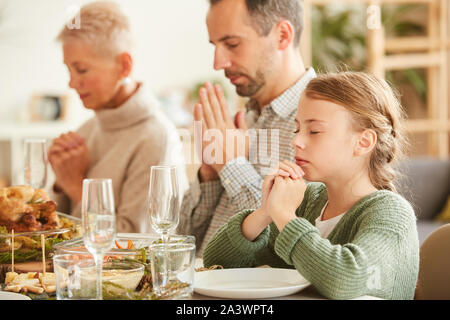 Famiglia di tre seduti al tavolo da pranzo con gli occhi chiusi e pregare prima di mangiare il pasto a casa Foto Stock