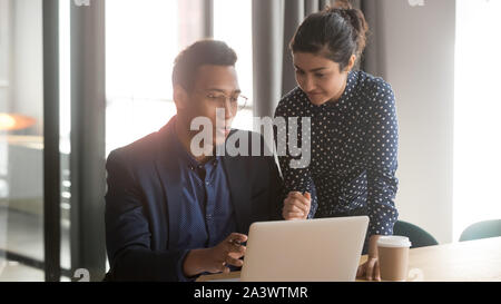 Mentor indiano collaboratore parlare aiutare nero intern spiegare il computer di lavoro Foto Stock