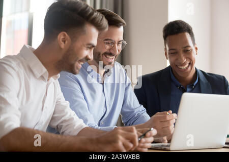 Happy business diversi team di uomini di ridere guardando il computer portatile Foto Stock