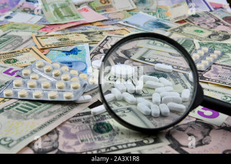 Magnifier, compresse e termometro su sfondo di diversi paesi moneta note. Il concetto di disponibilità di medico e di medico crescente exp Foto Stock
