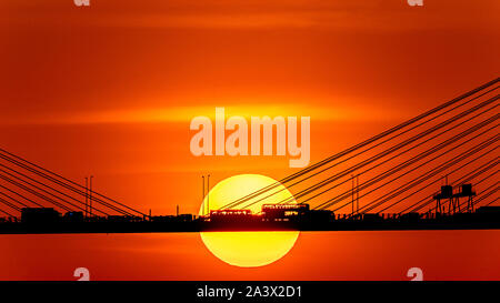 Tramonto sul cavo alloggiato a ponte con silhouette di automobile attraversando la baia mare Foto Stock