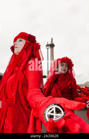 Estinzione clima di ribellione i manifestanti hanno proseguito la loro carriera di Trafalgar Square per un quarto giorno, con alcuni super-incollaggio le loro mani per la strada per bloccare il traffico. La polizia ha usato un JCB con un cherry picker per rimuovere gli attivisti da una torre di legno che era stato posto al centro della strada. Foto Stock