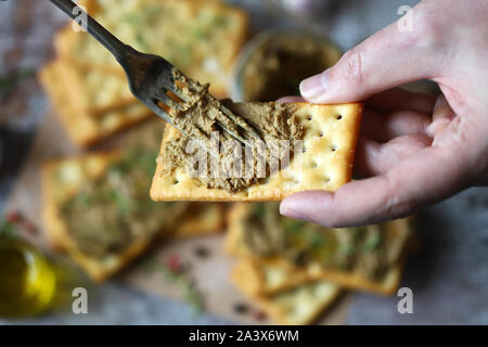 Maschio di mettere le mani la casa il patè di fegato su un cracker con una forchetta. Deliziosa casa pate con erbe e spezie. Dieta cheto. Cibo sano. Messa a fuoco selettiva. Foto Stock