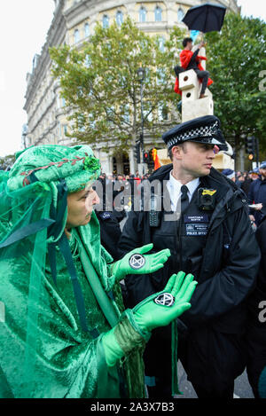 Londra, Regno Unito. Il 10 ottobre 2019. Membri del rosso e verde brigata, sostenitori di estinzione della ribellione, marzo silenziosamente intorno a forze di polizia che hanno circondato la struttura in legno che contiene gli attivisti fissato ad esso in Trafalgar Square durante il giorno 4 di estinzione Rebellion cambiamenti climatici protesta nella capitale. Gli attivisti chiedono al governo di prendere provvedimenti immediati contro le conseguenze negative del cambiamento climatico. Credito: Stephen Chung / Alamy Live News Foto Stock