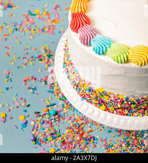 Vista aerea di una torta di compleanno con glassa di arcobaleno colorato e spruzza su uno sfondo blu. Foto Stock