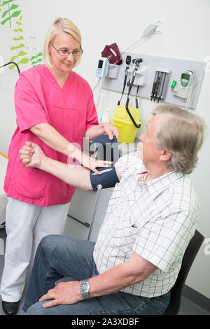 Femmina infermiera registrata la misura della pressione del sangue di un uomo anziano in un ospedale Foto Stock