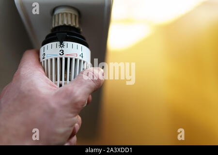 Mano di uomo regolazione valvola del termostato del radiatore al numero tre icona (posizione centrale), simbolo per risparmiare soldi a spese di riscaldamento o la temperatura media Foto Stock