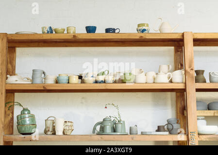 Fatte a mano di ceramica in una bottega del vasaio. Piastre di argilla, tazze e teiere sui ripiani in officina studio. Foto Stock