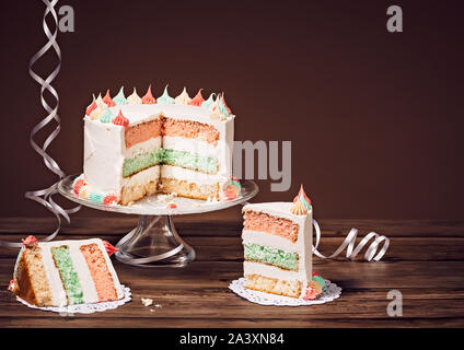 Fette di torta di compleanno con tre color pastello strati su uno sfondo marrone Foto Stock