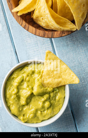 Il mais nacho chips e avocado dip. Giallo tortilla chips e guacamole nella ciotola sul tavolo blu. Foto Stock