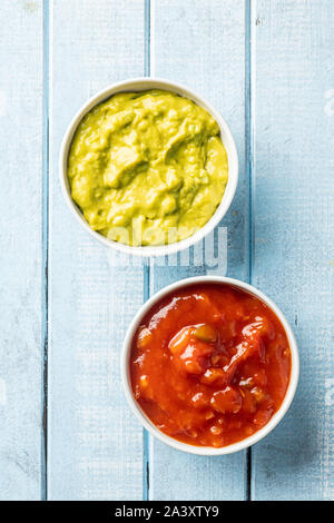 Salse in ciotola. Guacamole e pomodoro dip sul tavolo blu. Vista dall'alto. Foto Stock