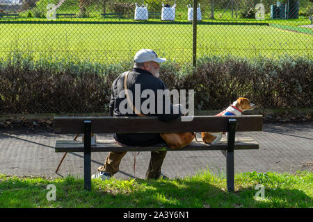 Un uomo seduto su una panchina nel parco con il suo cane Foto Stock