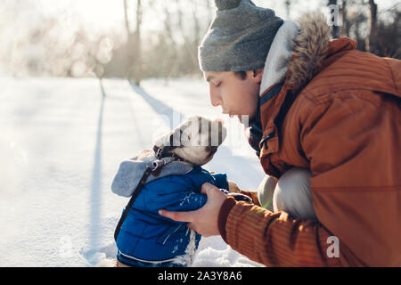 Pug dog passeggiate sulla neve con il suo maestro. Cucciolo indossando cappotto invernale Uomo di baciare il suo pet nella foresta di inverno Foto Stock
