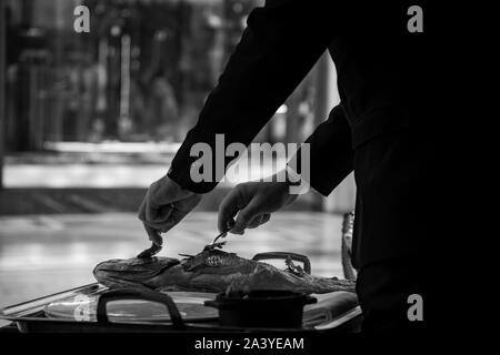 Un esperto cameriere che serve una deliziosa orata di mare alla griglia in un elegante ristorante. Foto Stock
