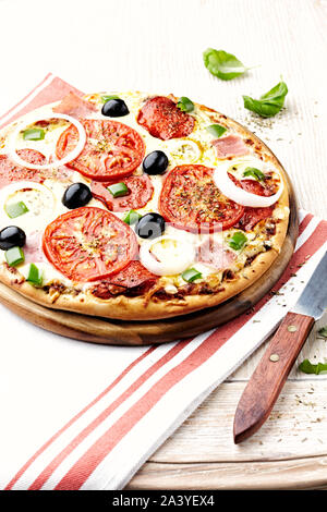 Pizza con salame, prosciutto, formaggio mozzarella, succosa pomodori, peperoni verdi, cipolla bianca, origano e basilico fresco. Foto Stock