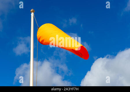 Un arancione manica a vento volare nella brezza su un palo di bandiera con un cielo blu dietro Foto Stock