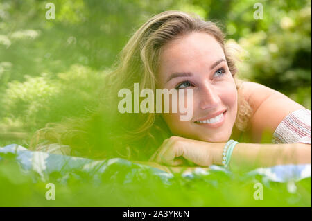 Sorridente giovane donna sdraiata in giardino Foto Stock